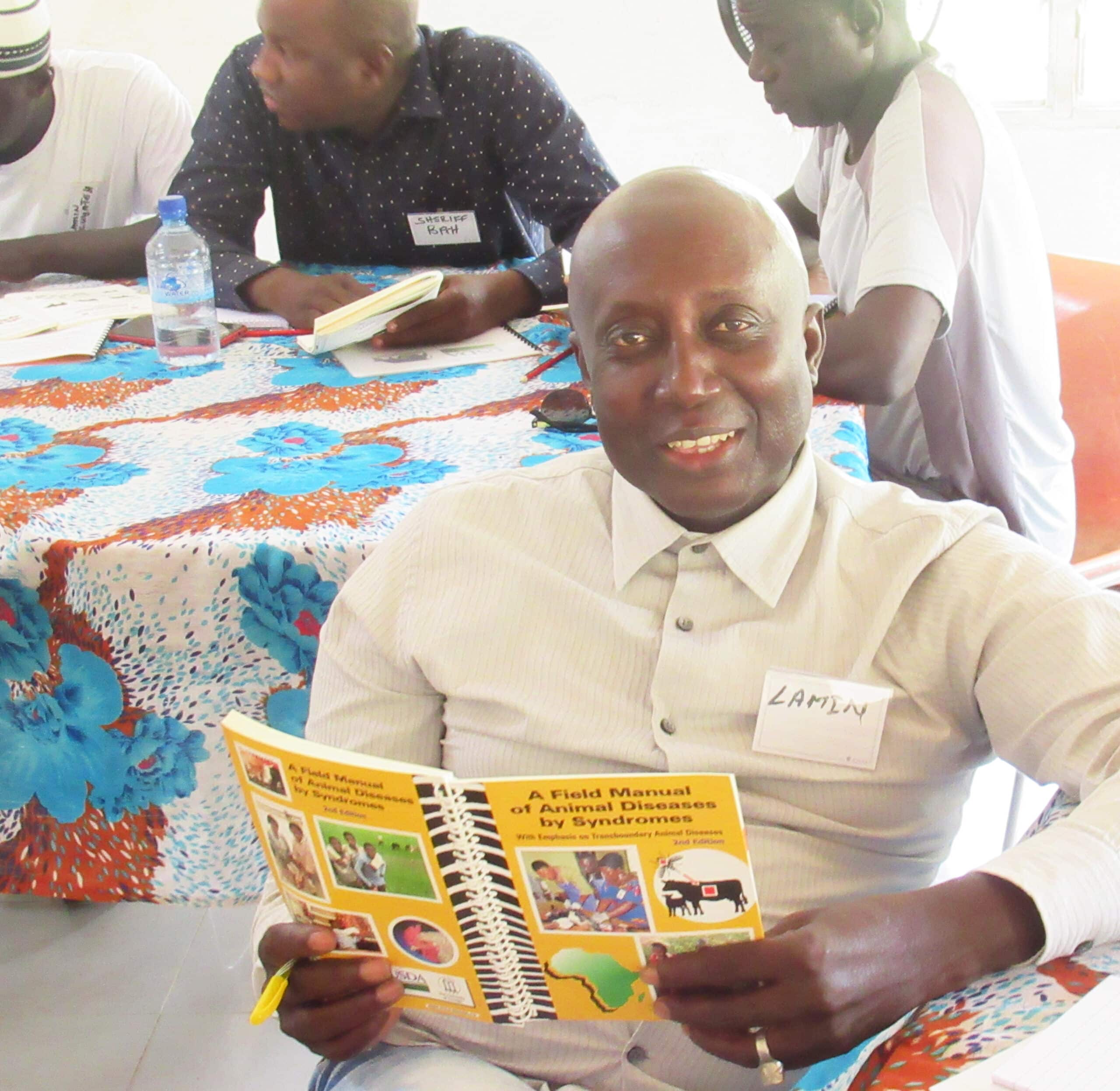 Training participant holds a field manual on animal diseases while seated with other attendees.